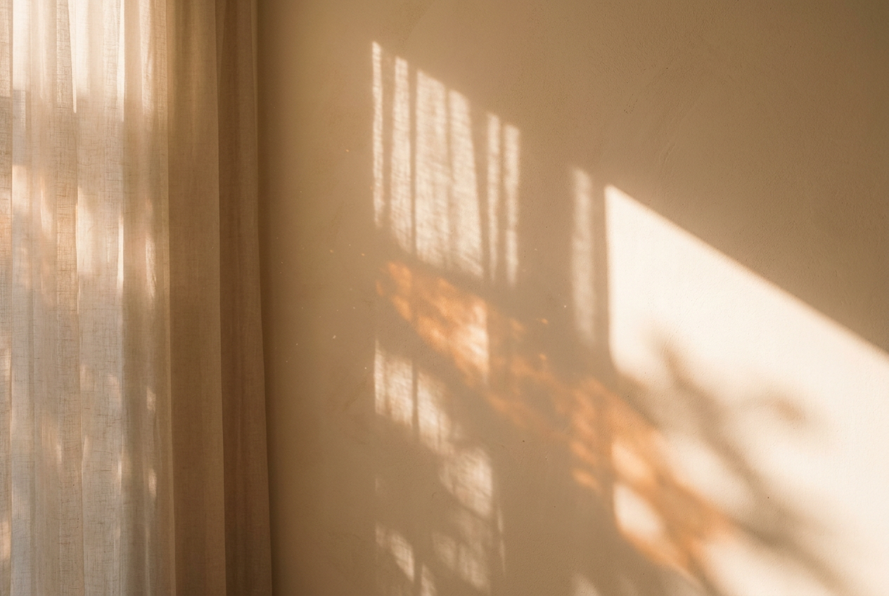 Warm golden morning sunlight streaming through a sheer linen curtain onto a cream wall