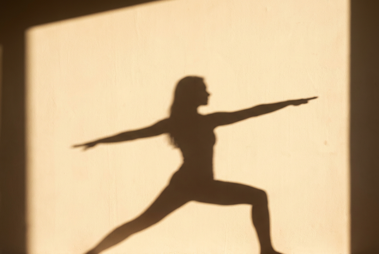 Shadow of a person in warrior yoga pose cast onto a warm cream wall in golden afternoon light
